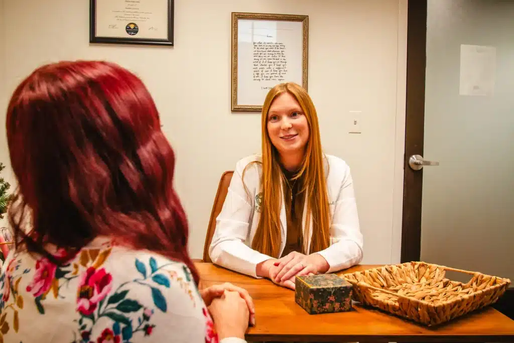 Two women are talking at a desk in an office setting.