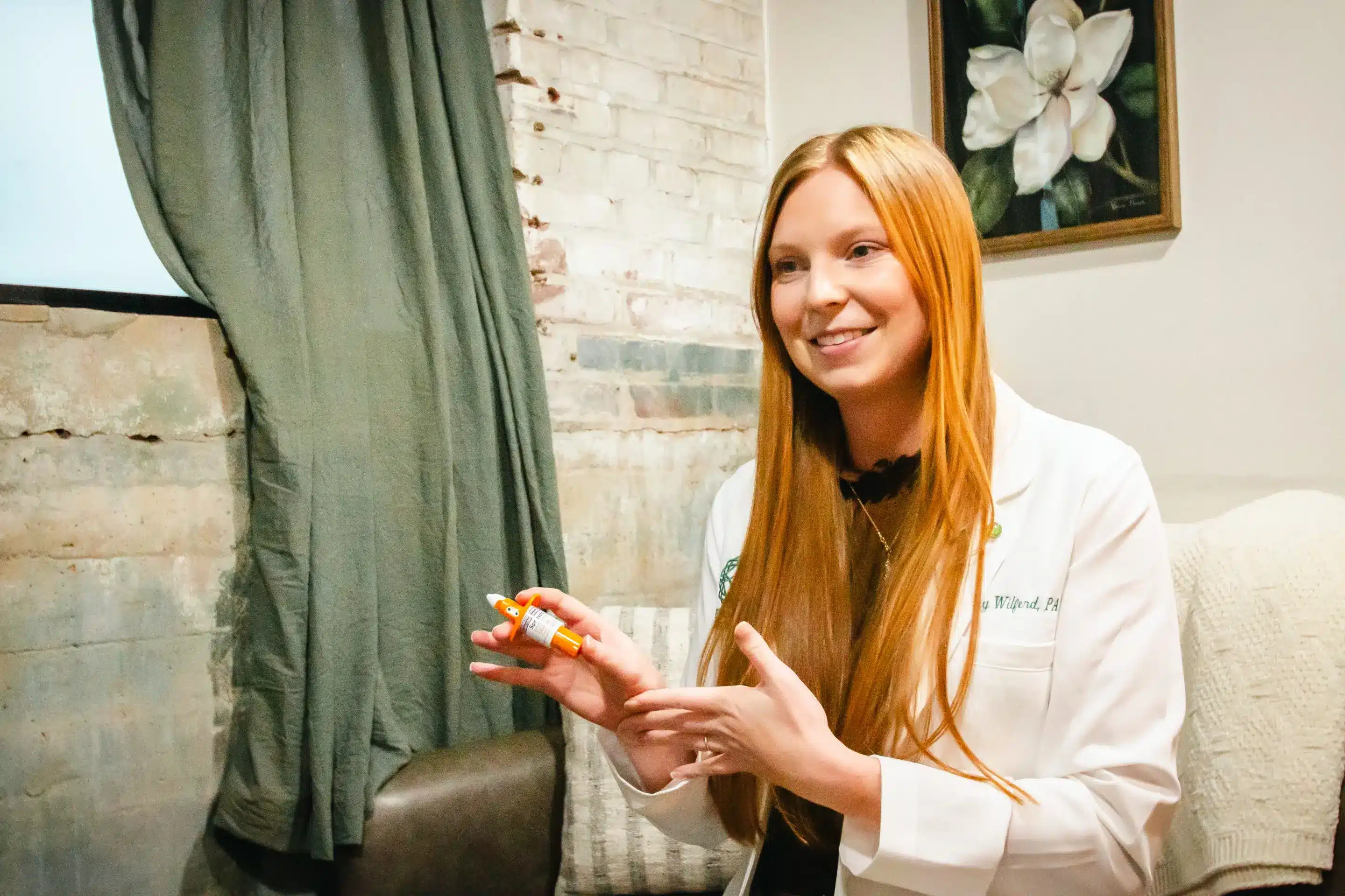 A woman in a lab coat holds a small device, smiling in a room with rustic decor.