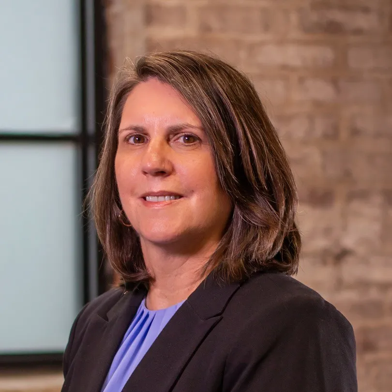 A woman in a blazer poses in front of a brick wall.