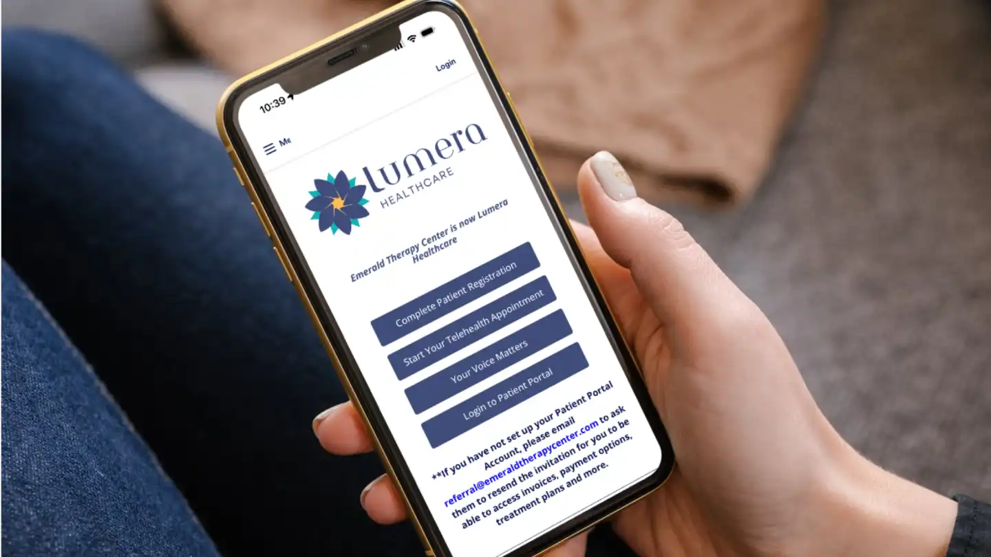 A person holds a smartphone displaying the Lumera Healthcare patient portal page.