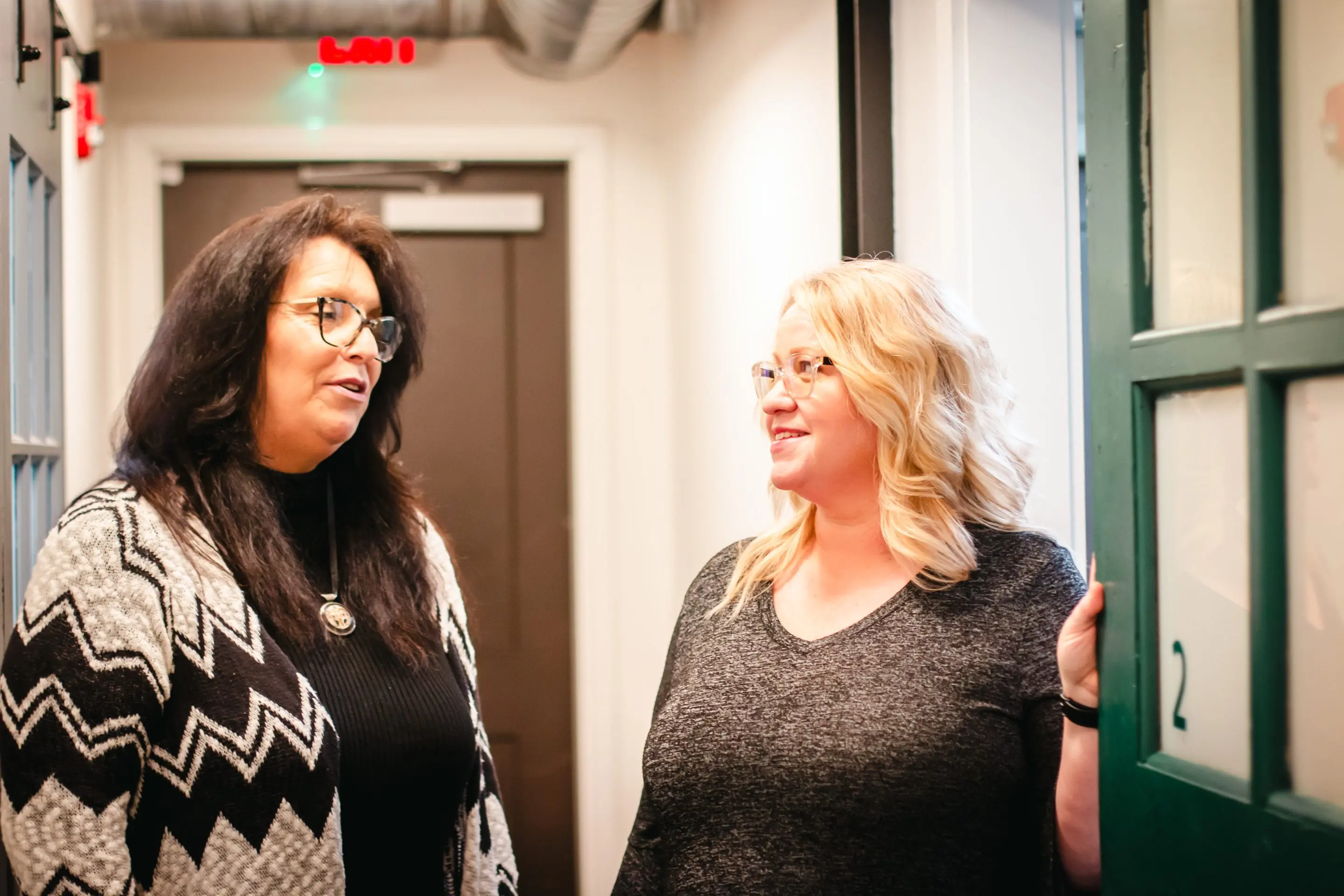 Two women stand in a hallway, engaged in conversation.