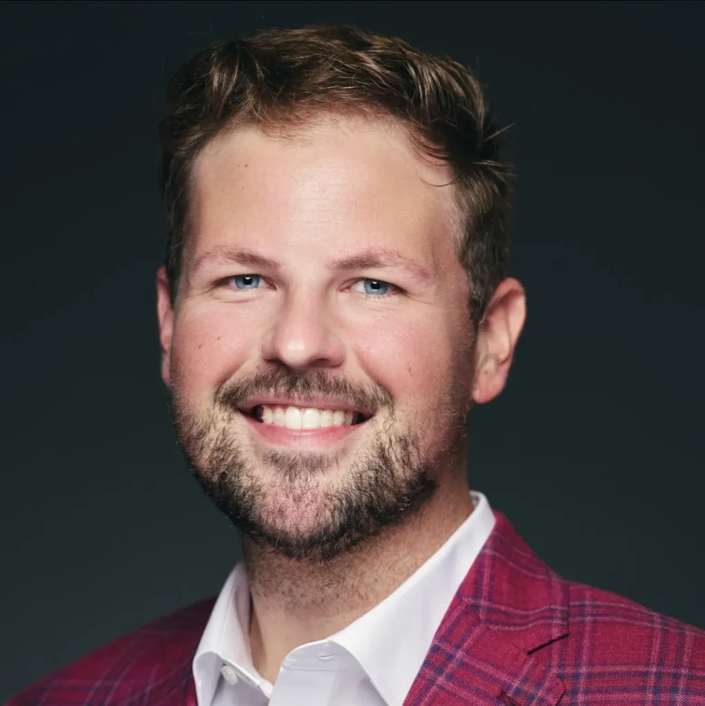 Smiling man in a red plaid suit against a dark background.