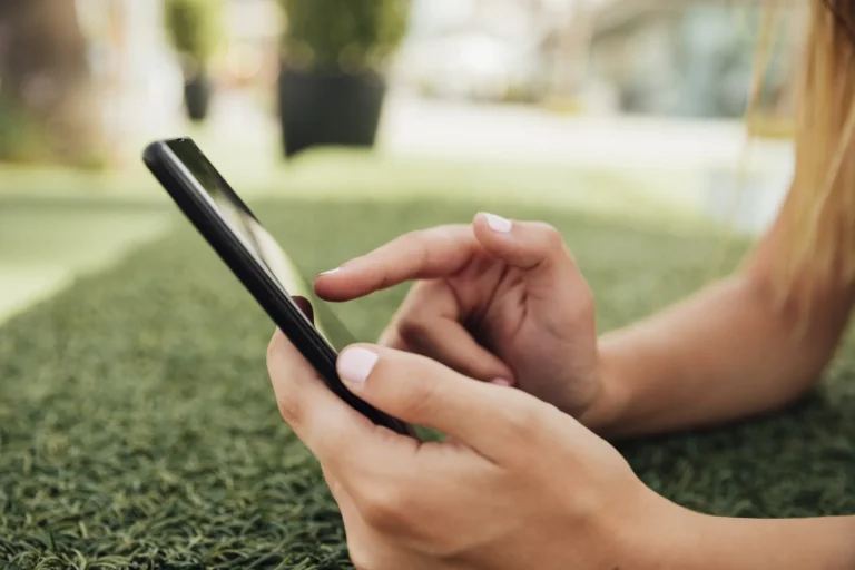 Person using a smartphone outdoors on grass.