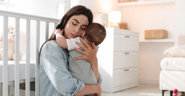 Tired mother holding and comforting her baby in a nursery, representing postpartum anxiety, emotional stress, and maternal mental health challenges after childbirth.