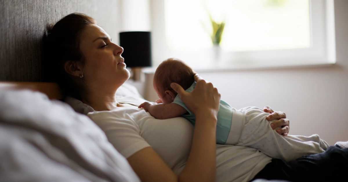 Mother resting in bed while holding her newborn baby, illustrating the emotional and physical symptoms associated with postpartum anxiety after childbirth.