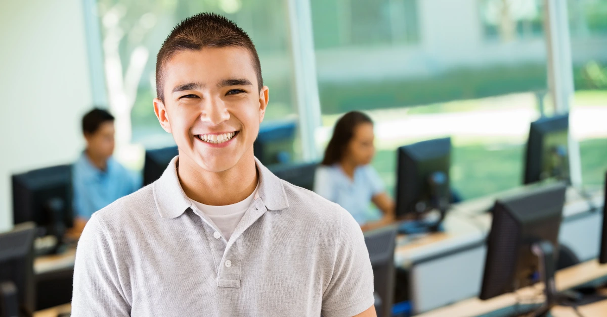 Smiling teenager in a classroom setting, representing the positive outcomes and academic support available through a teen intensive outpatient program (IOP) for mental health.
