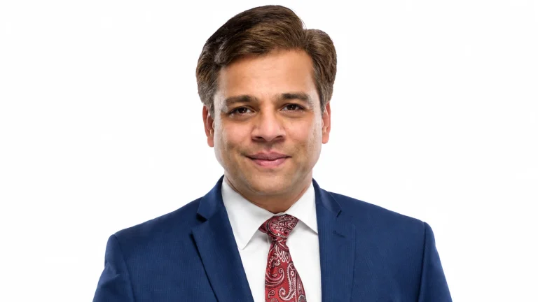 Manish Sood smiling in a blue suit and red paisley tie