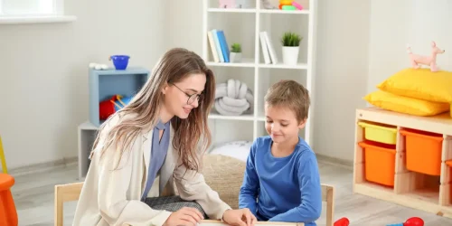 Child therapist working one-on-one with a young boy during a pediatric mental health counseling session in a play therapy room.