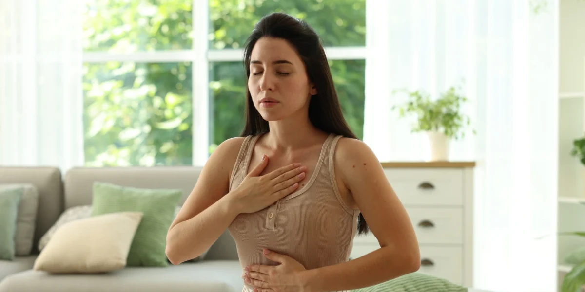 Woman practicing deep breathing with one hand on her chest and one on her abdomen, illustrating coping techniques for panic attacks and anxiety attacks.