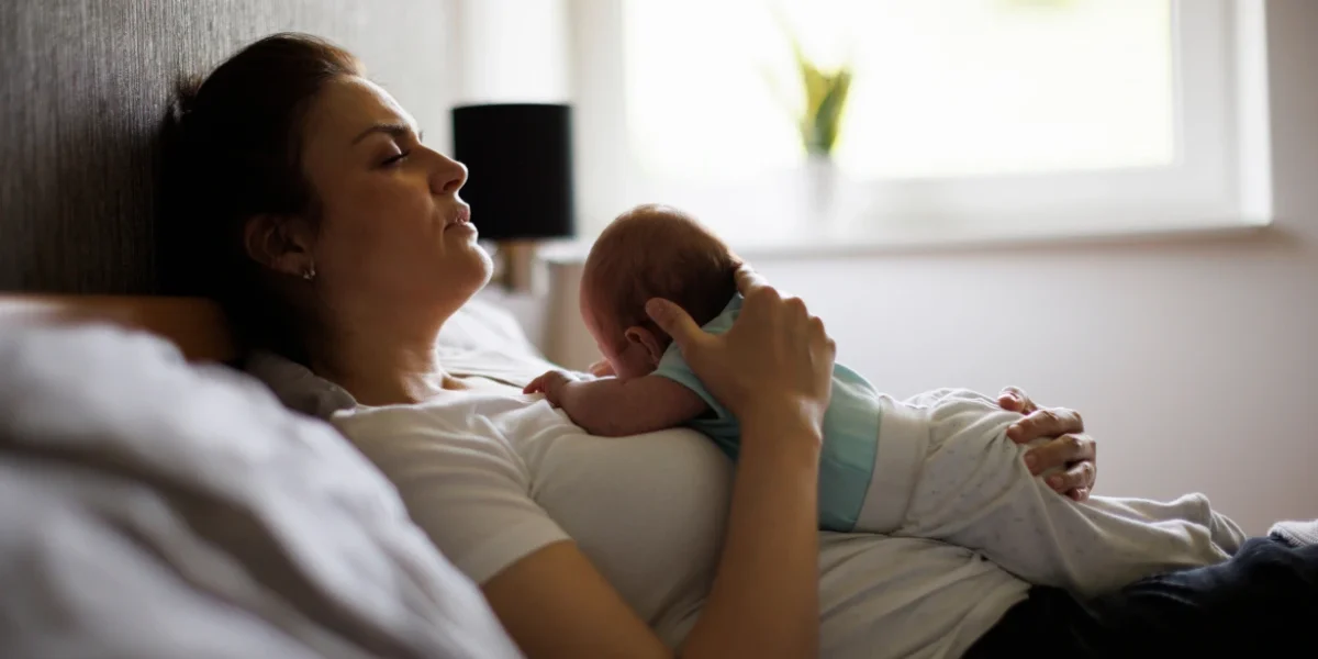 Mother resting in bed while holding her newborn baby, illustrating the emotional and physical symptoms associated with postpartum anxiety after childbirth.