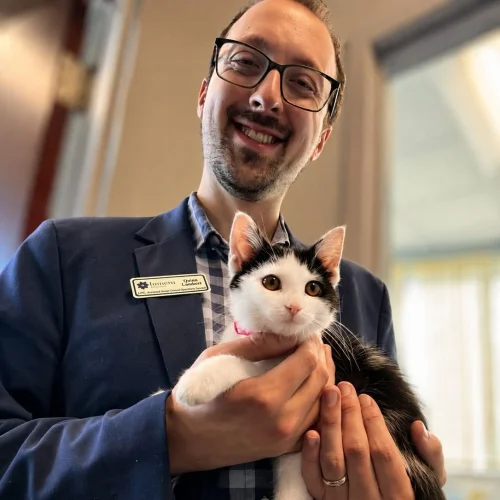 Quinn Lambert smiling while holding a black-and-white cat, highlighting the comforting role of animals in a supportive care environment.