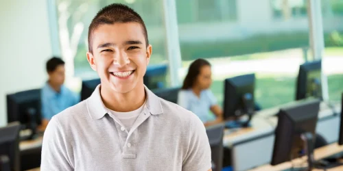 Smiling teenager in a classroom setting, representing the positive outcomes and academic support available through a teen intensive outpatient program (IOP) for mental health.